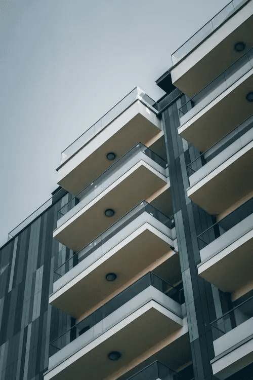 Modern apartment building with stacked balconies viewed from below against a pale sky